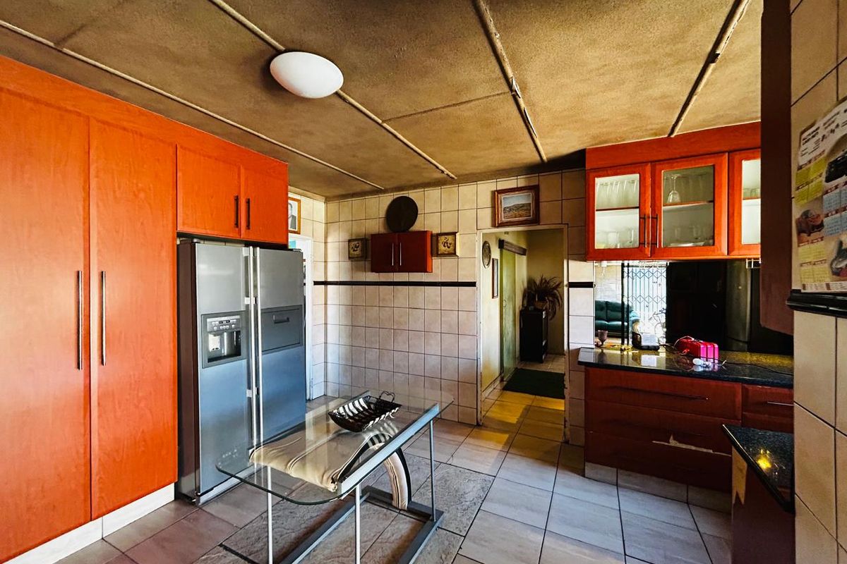 A dated kitchen featuring orange-toned cabinetry, granite countertops, and tiled flooring, offering a functional layout with potential for modern renovation.
