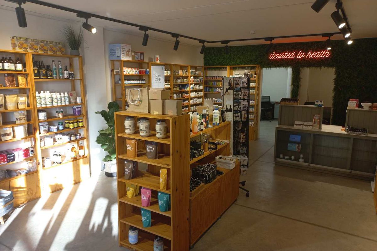 A well-lit retail space featuring custom wooden shelving units, a service counter, and a decorative artificial green wall with neon signage.