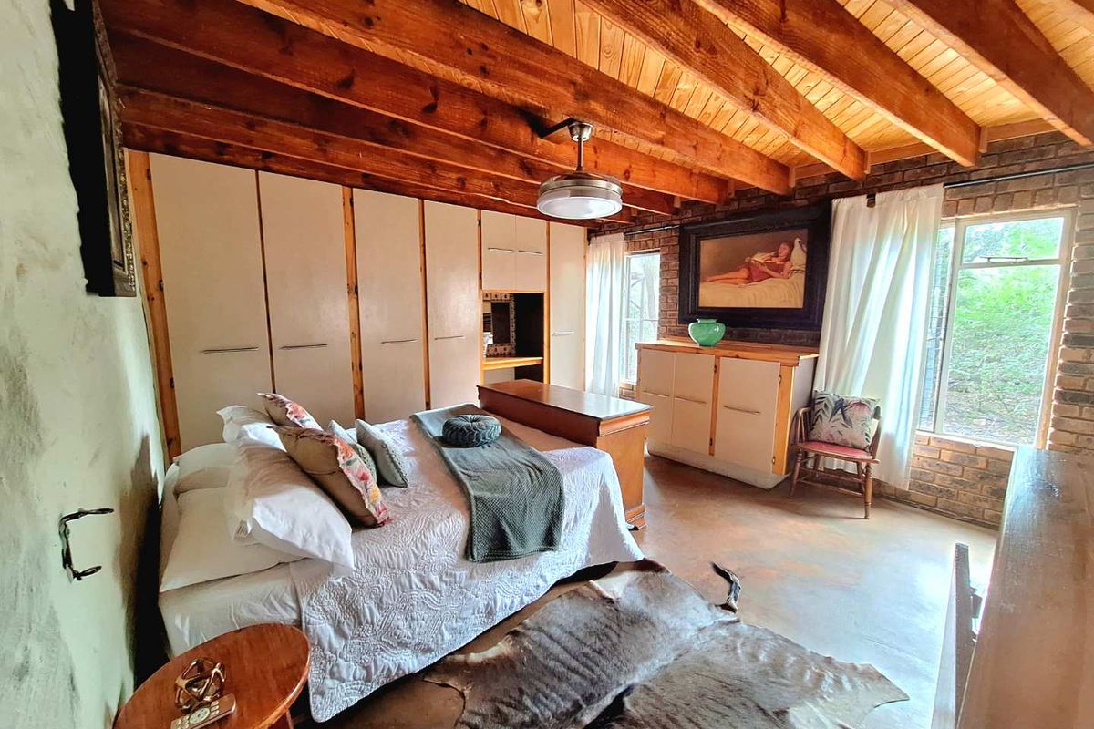 Spacious bedroom featuring exposed timber beam ceilings, face-brick feature walls, and extensive built-in wardrobe storage with a neutral aesthetic.