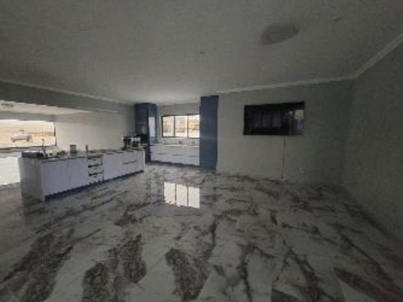 Spacious open-plan living and kitchen area featuring polished marble-look floor tiles, modern built-in cabinetry, and a central kitchen island.
