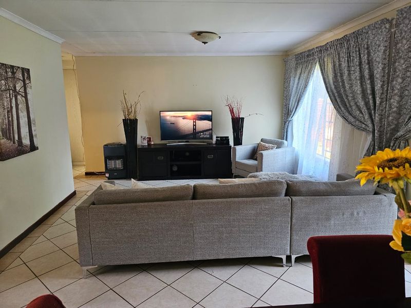 A comfortable living room featuring tiled flooring and large windows with curtains, providing a functional and well-lit space for relaxation.