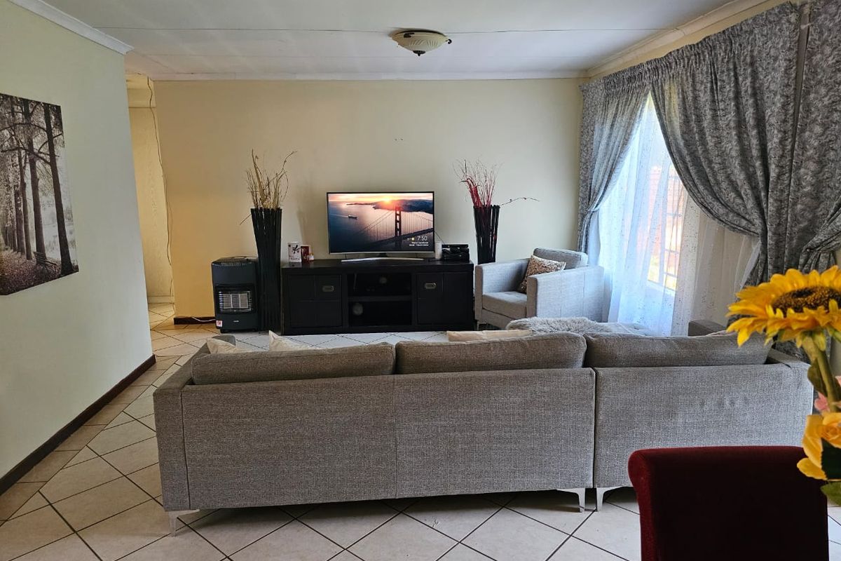 A comfortable living room featuring tiled flooring and large windows with curtains, providing a functional and well-lit space for relaxation.