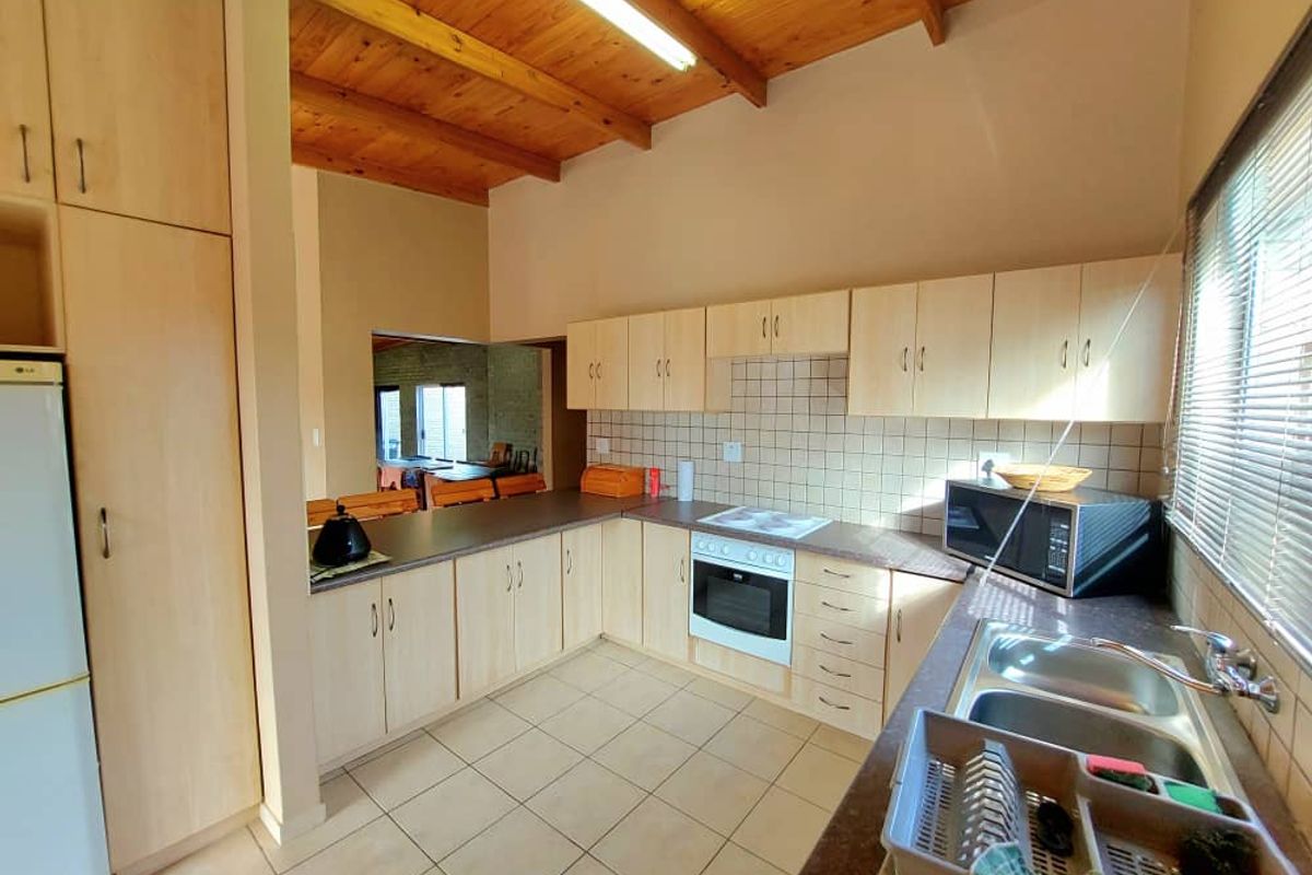 Functional kitchen featuring light wood cabinetry, tiled splashback, built-in oven, hob, and double basin sink under a high timber-beamed ceiling.