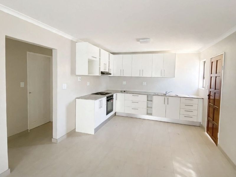 A clean, modern kitchen featuring white cabinetry, stone countertops, built-in oven, hob, and tiled flooring in an open-plan layout.