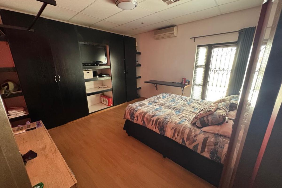 A bedroom featuring laminate flooring, built-in black cabinetry, an air conditioning unit, and a security gate leading to the exterior.
