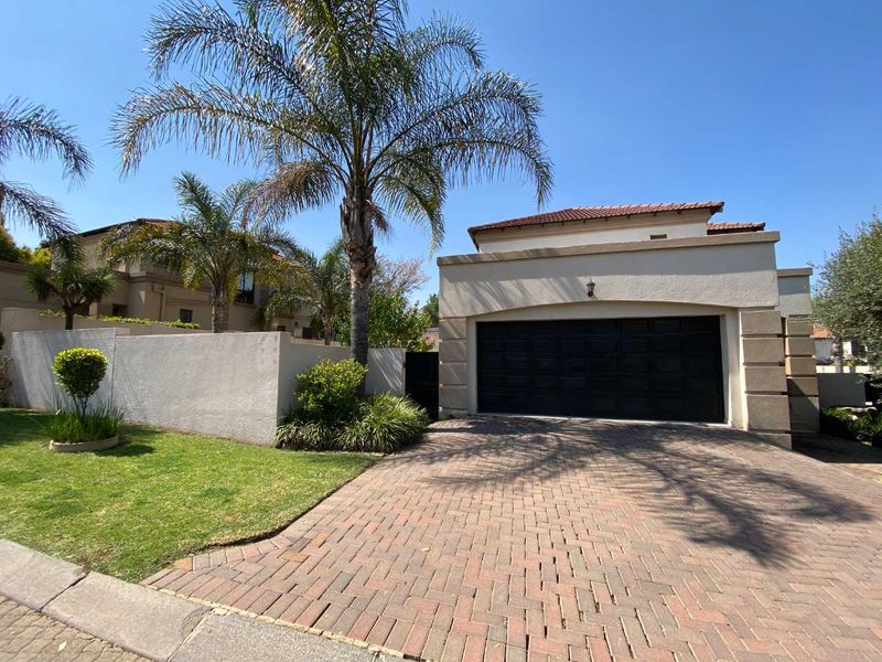 Front view of the property featuring a paved driveway, double garage, and well-maintained boundary wall with established landscaping.