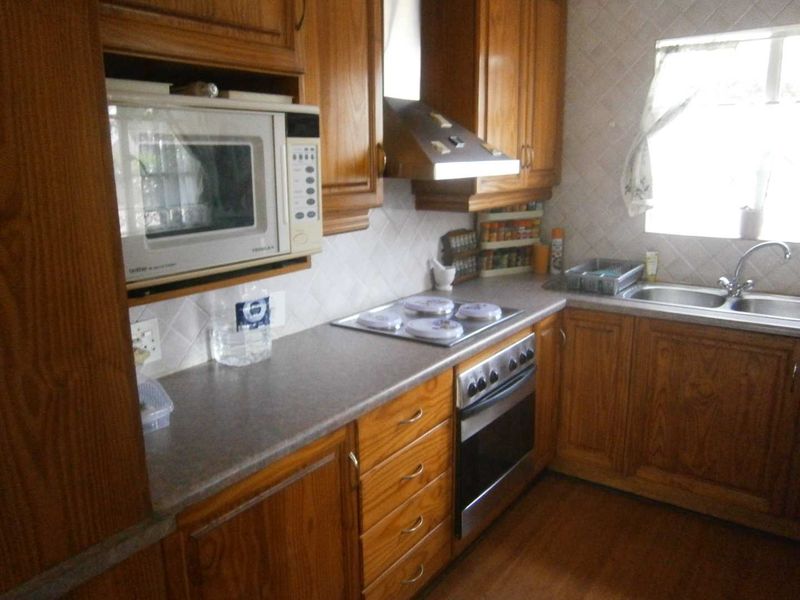 A functional kitchen featuring traditional wooden cabinetry, laminate countertops, a built-in oven with hob, and a double bowl sink with tiled backsplash.
