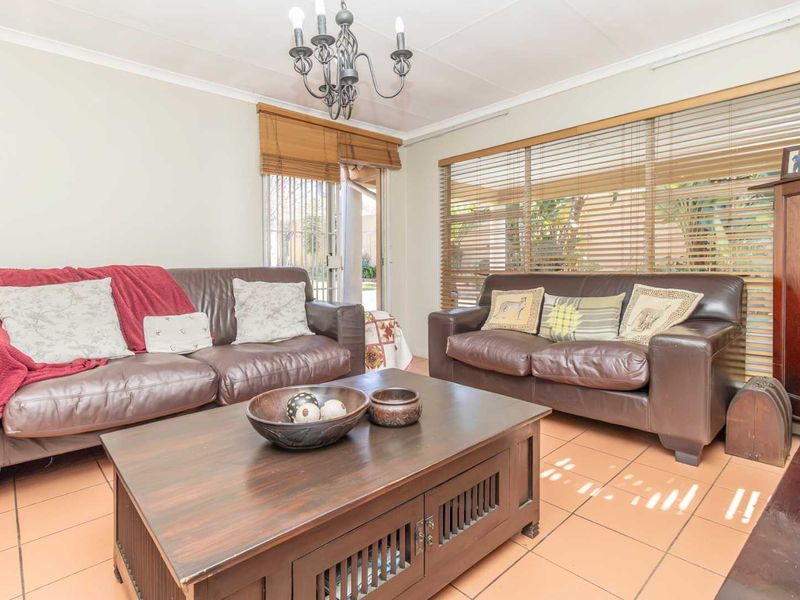 A comfortable living room featuring tiled flooring, a sliding glass door providing outdoor access, and natural light filtered through venetian blinds.