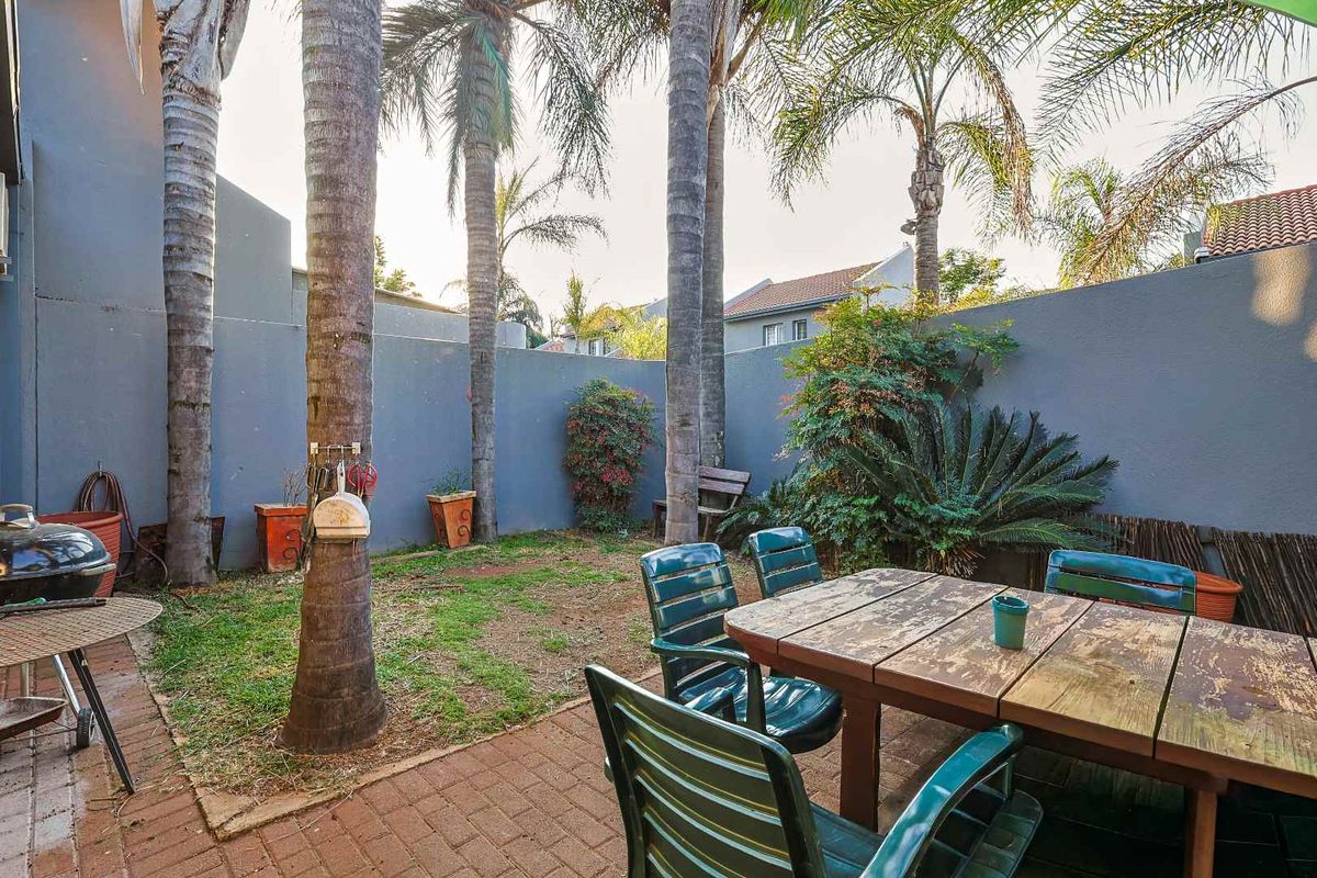A private rear garden featuring a paved patio area, established palm trees, and perimeter boundary walls, offering a functional outdoor space.