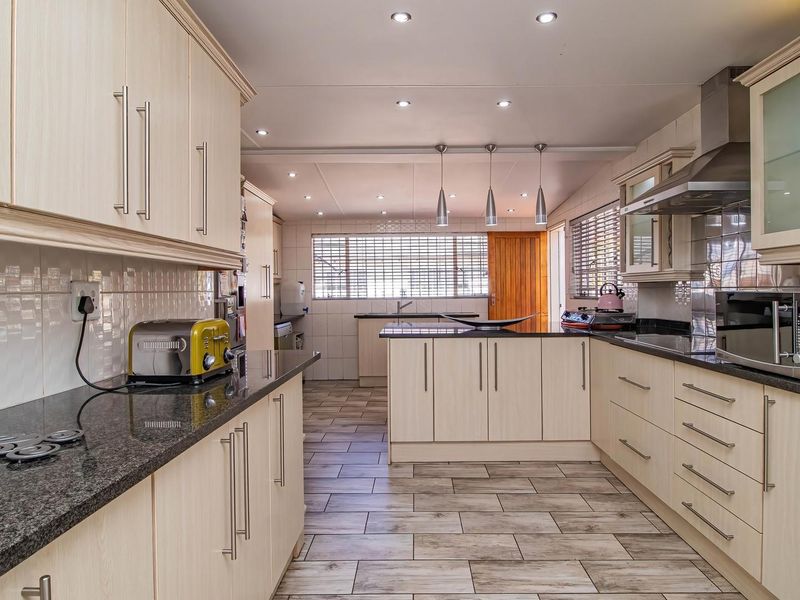 A well-appointed kitchen featuring light wood cabinetry, granite countertops, integrated appliances, and modern tiled flooring with ample workspace and recessed lighting.