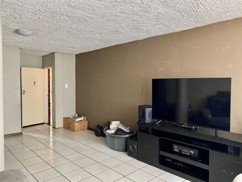 A living room area featuring tiled flooring and a textured ceiling, currently requiring cosmetic updates to the wall finishes.