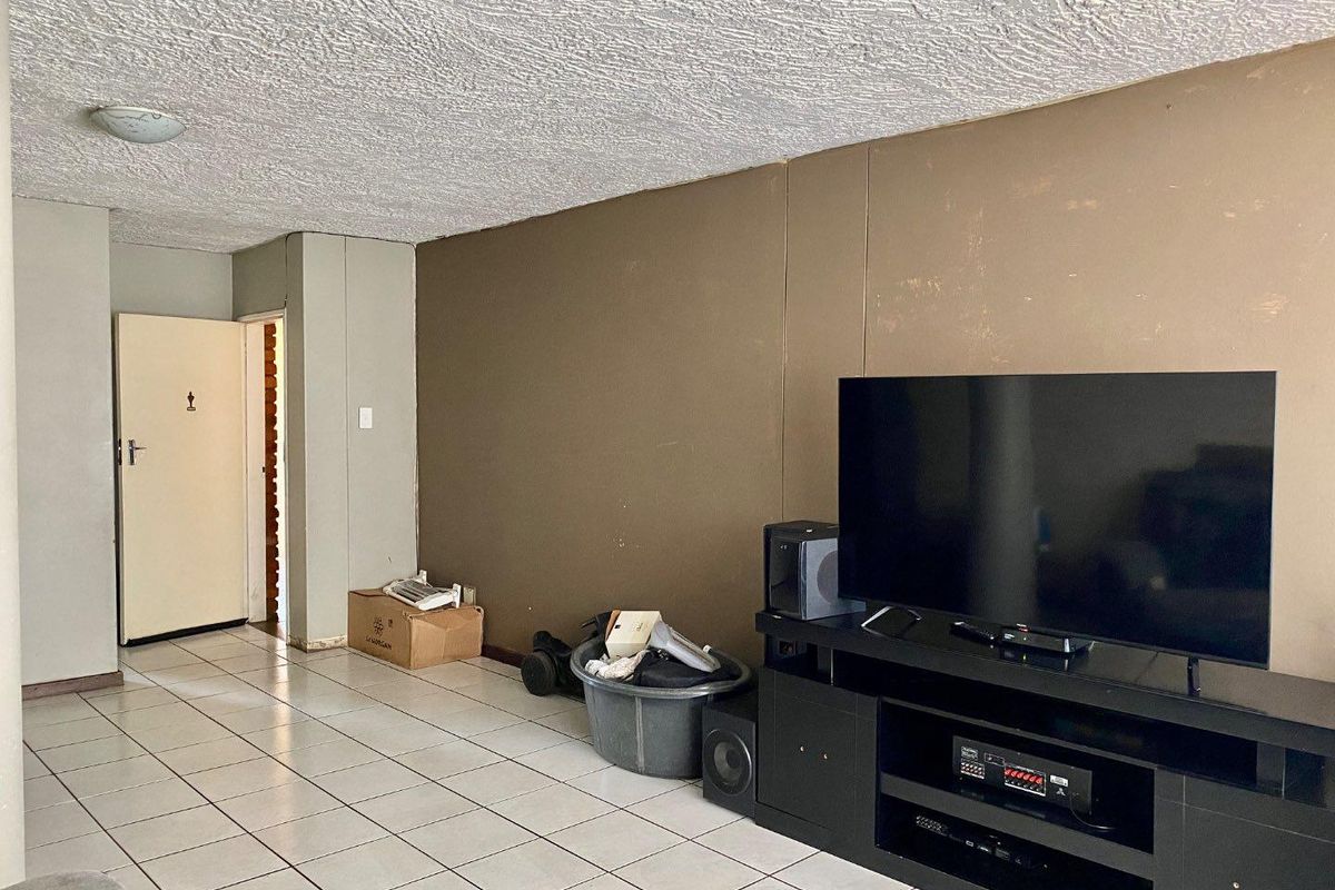 A living room area featuring tiled flooring and a textured ceiling, currently requiring cosmetic updates to the wall finishes.