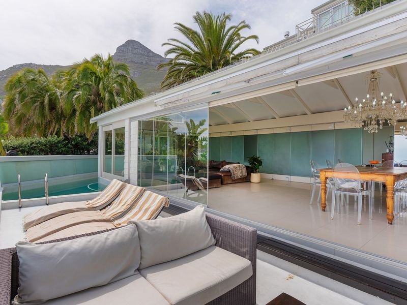Spacious covered patio area featuring seamless glass sliding doors, tiled flooring, and direct access to an adjacent swimming pool with mountain views.