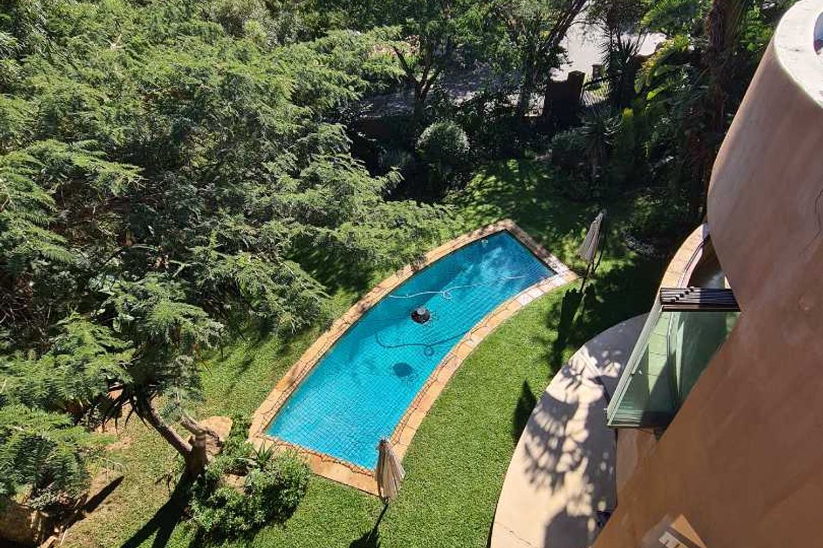 Elevated aerial view of a private garden featuring a curved swimming pool, lush landscaping, and a balcony overlooking the outdoor space.