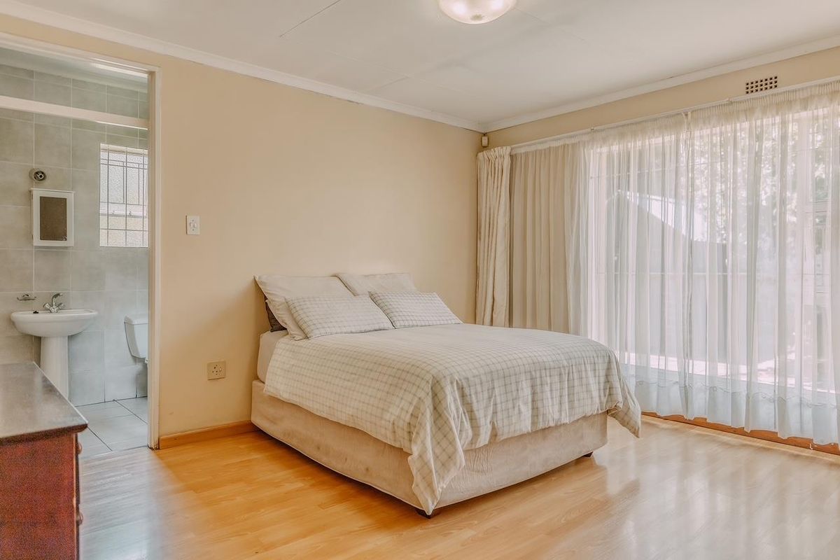 A bedroom featuring light wood-look flooring, large sliding glass doors with curtains, and an en-suite bathroom with tiled walls and a pedestal basin.