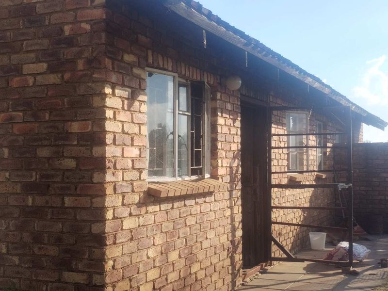 Rear view of a face brick farm building featuring steel window frames, a security gate, and visible wear to the roof eaves.