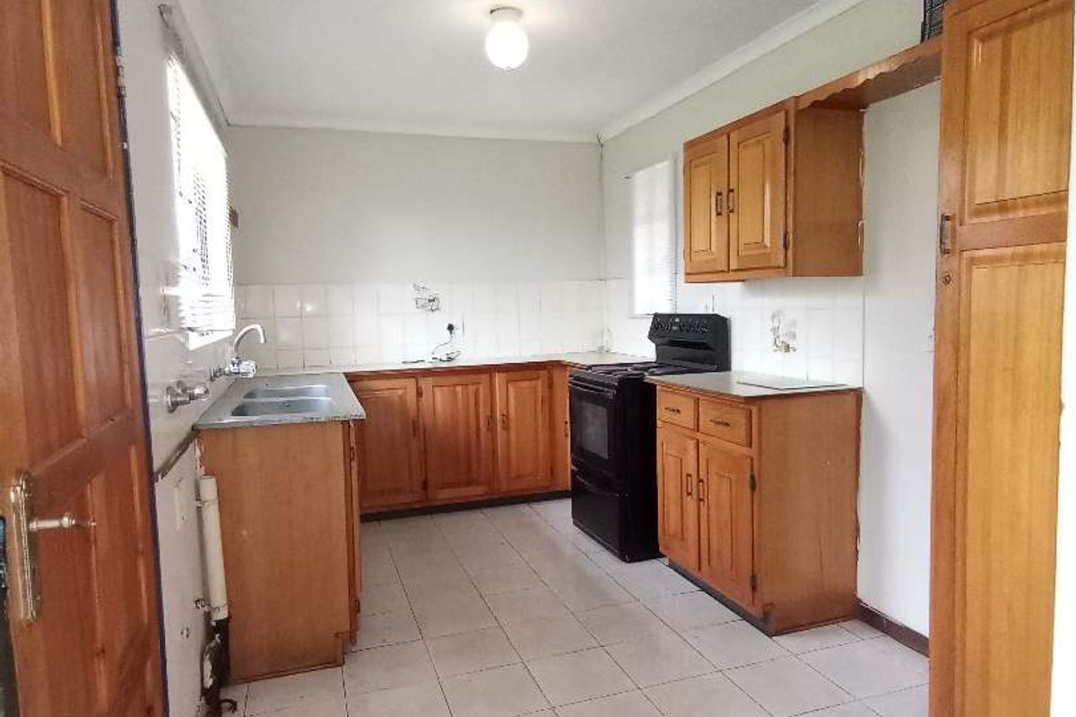A functional kitchen featuring wooden cabinetry, tiled flooring, a double basin sink, and a freestanding stove.