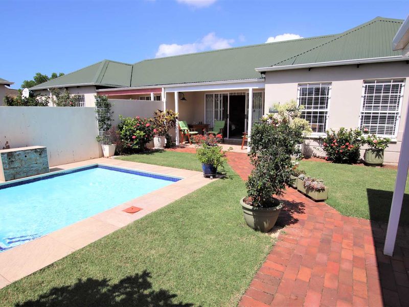 Rear exterior view of the townhouse featuring a private swimming pool, brick paved walkway, covered patio area, and a well-maintained garden.