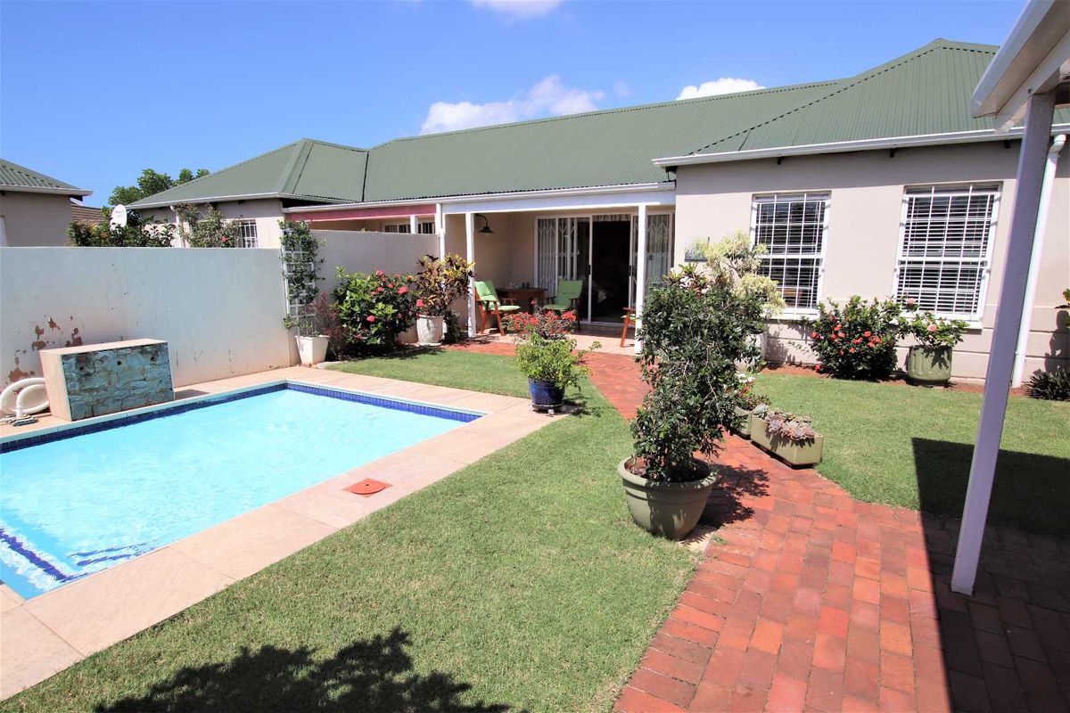Rear exterior view of the townhouse featuring a private swimming pool, brick paved walkway, covered patio area, and a well-maintained garden.