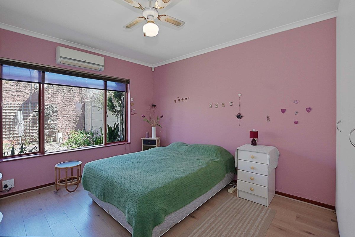 A bedroom featuring laminate flooring, a ceiling fan, and a wall-mounted air conditioning unit, with a large window overlooking the rear garden area.