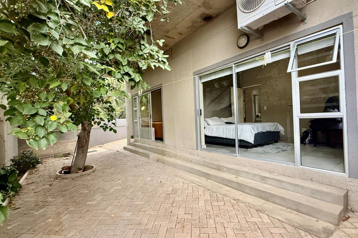 Exterior view of an apartment patio featuring paved flooring, sliding glass doors, and an integrated air conditioning unit.