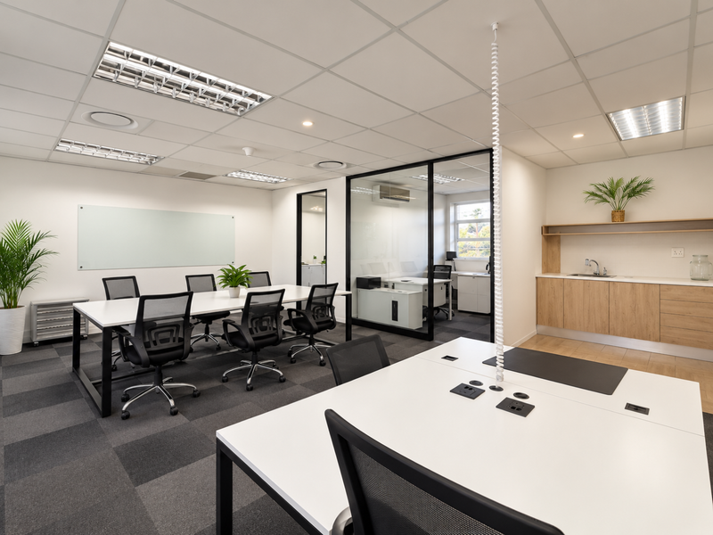 Modern open-plan office space featuring a glass-partitioned meeting room, built-in kitchenette, suspended ceilings, and professional carpet tile flooring.