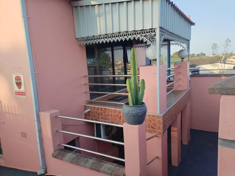 An elevated balcony featuring a stainless steel balustrade, decorative metal fretwork, and tiled flooring, providing an outdoor space with a corrugated metal roof.