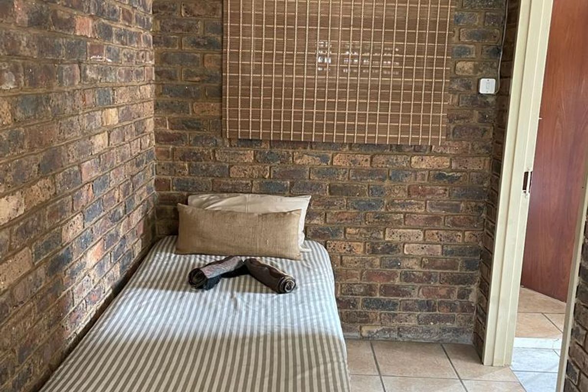A compact bedroom featuring exposed face-brick walls and tiled flooring, providing a rustic and functional living space.