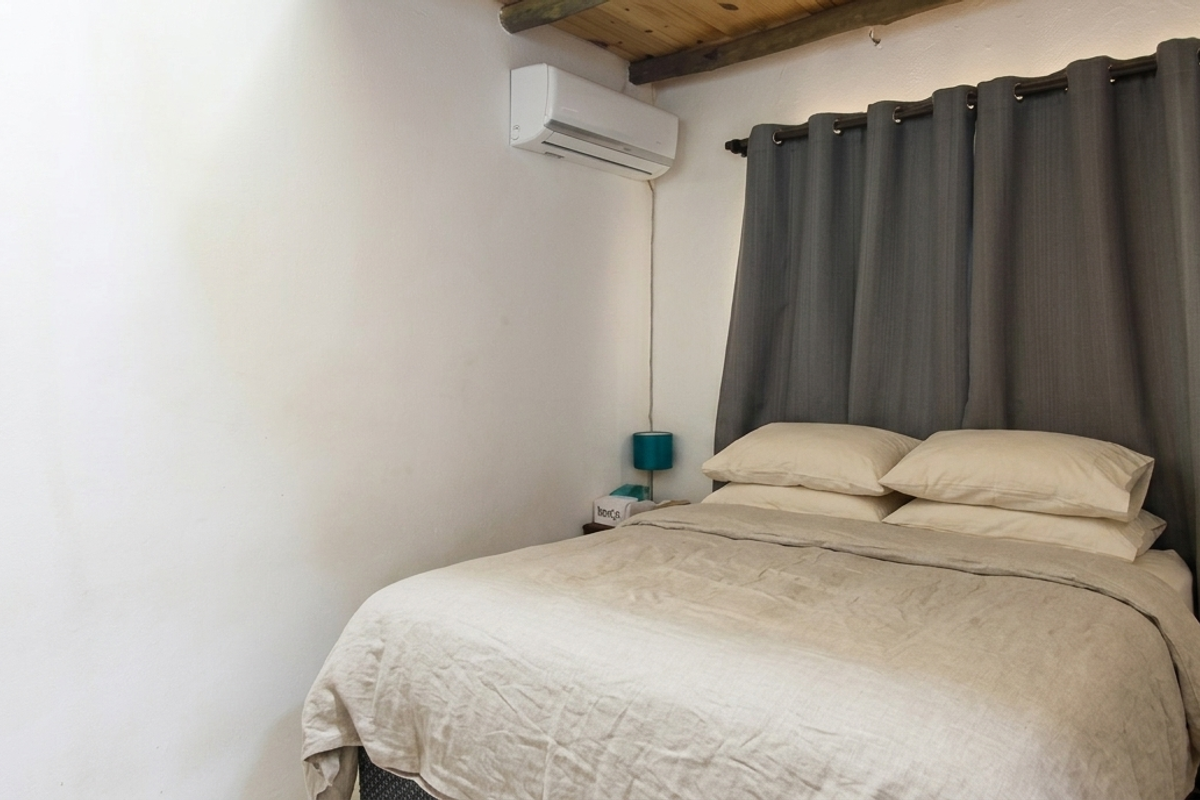 A cozy bedroom featuring exposed timber ceiling beams and a wall-mounted air conditioning unit.