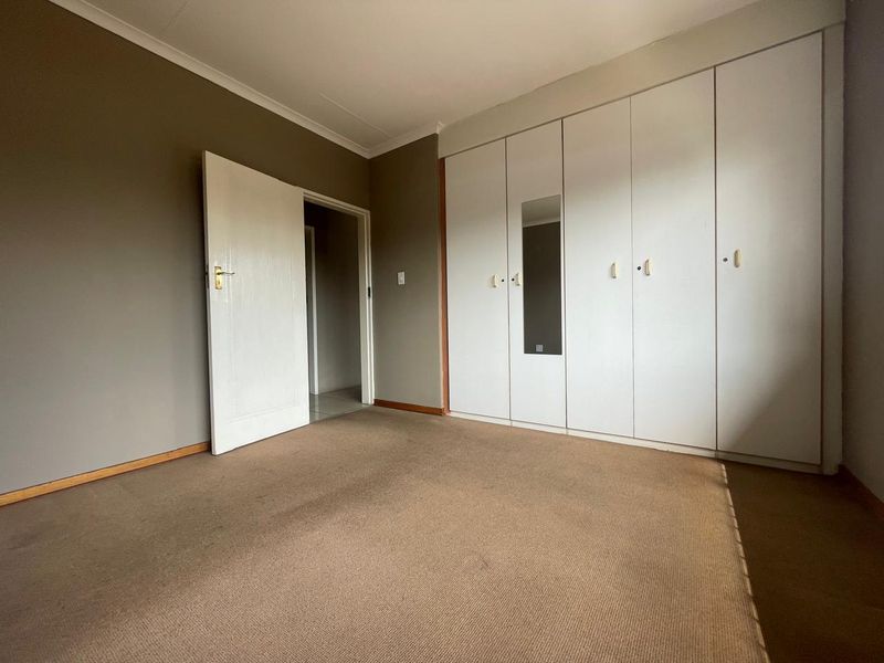 A vacant bedroom featuring neutral wall tones, carpeted flooring, and a large wall-to-wall built-in cupboard unit with a central mirror.