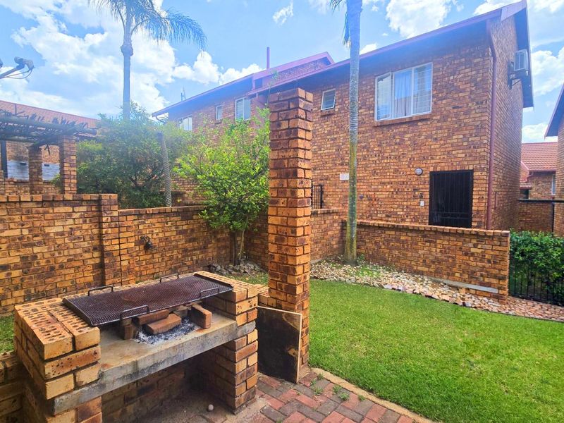 Rear exterior view of the townhouse featuring a private garden, brick-built braai area, and paved patio space.