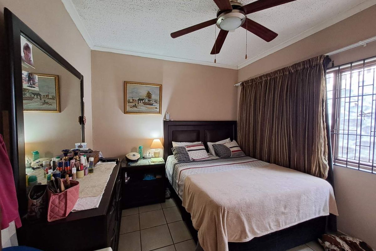 A bedroom featuring tiled flooring, a ceiling fan, and security bars on the window.