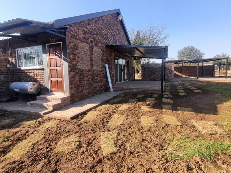 Rear view of a face brick house featuring a covered patio, paved walkway, and an external gas geyser unit set within an unfinished garden area.