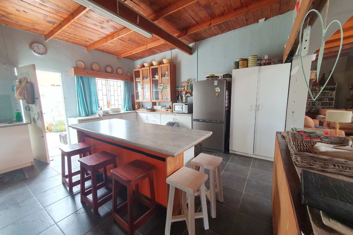 Spacious kitchen featuring a central island with breakfast bar, exposed timber beam ceiling, and ample built-in cabinetry with direct access to the exterior.
