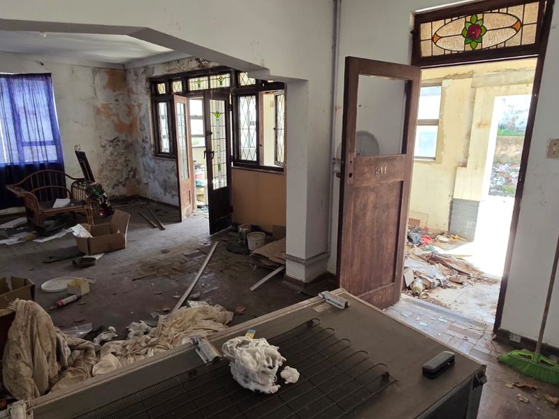 A dilapidated living area featuring an archway and stained glass detailing, requiring significant renovation and repair to restore the interior finishes.