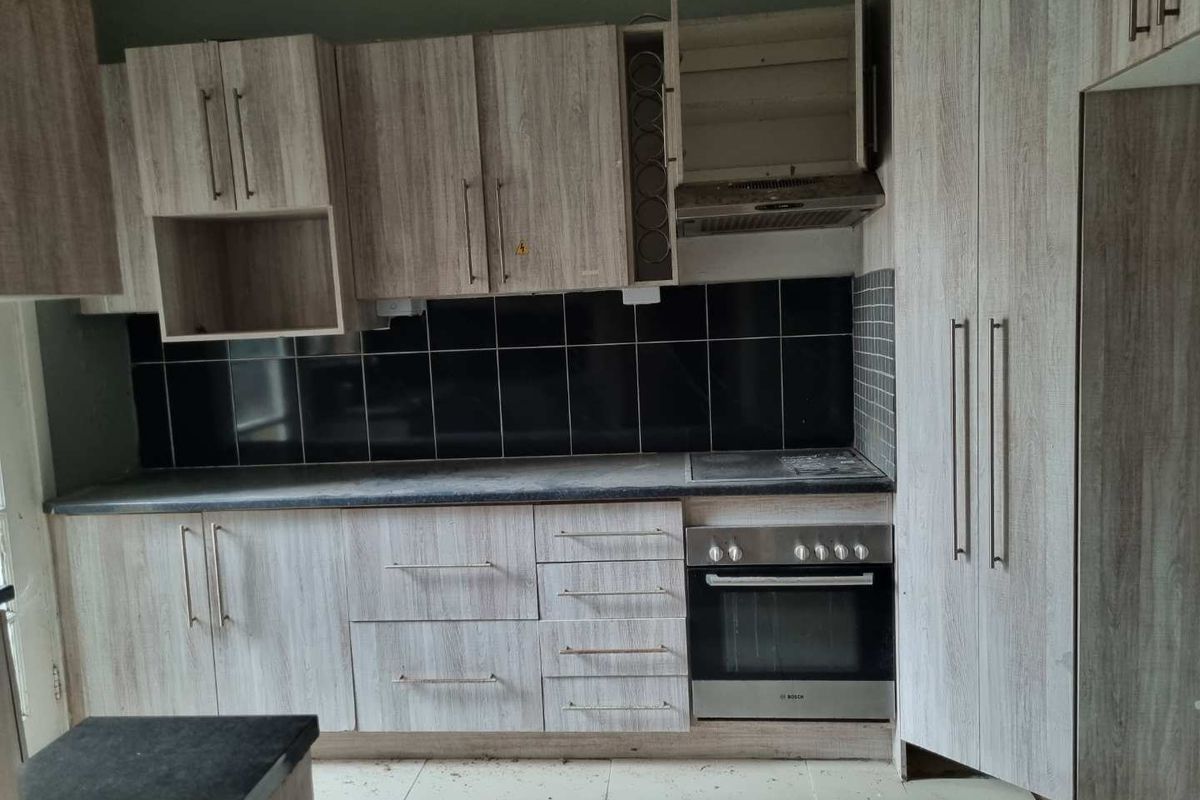 A vacant kitchen featuring wood-look cabinetry, a black tiled backsplash, built-in oven, and extractor fan, requiring minor repairs and cleaning.