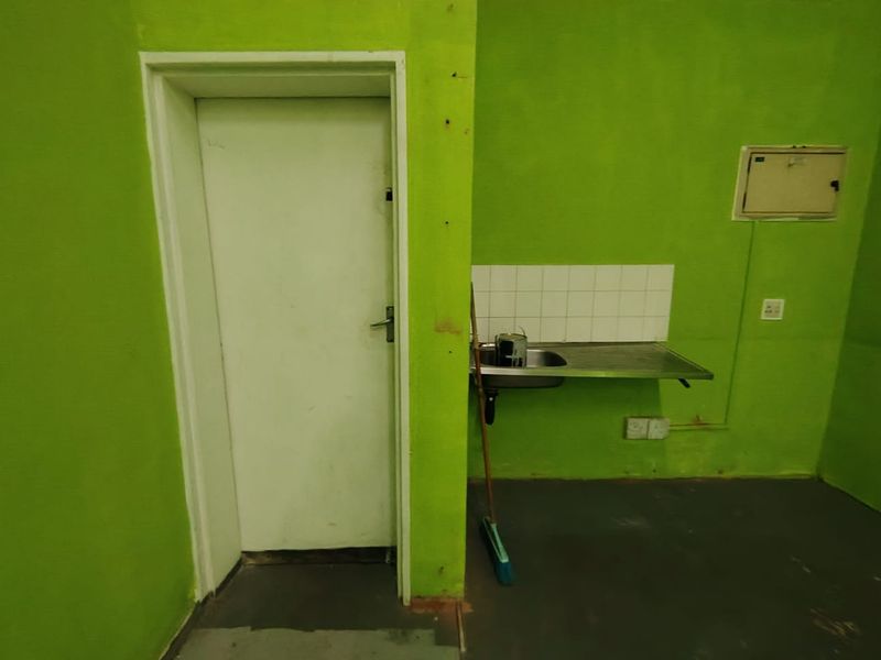 A basic kitchenette area featuring a stainless steel sink, tiled splashback, and a doorway, requiring cosmetic updates to improve the space.