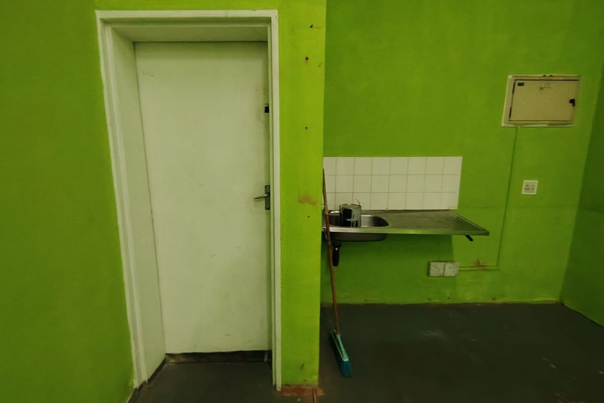 A basic kitchenette area featuring a stainless steel sink, tiled splashback, and a doorway, requiring cosmetic updates to improve the space.