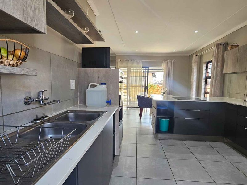 Modern open-plan kitchen featuring sleek cabinetry, stone countertops, double sink, and tiled flooring, flowing seamlessly into the living area with natural light.