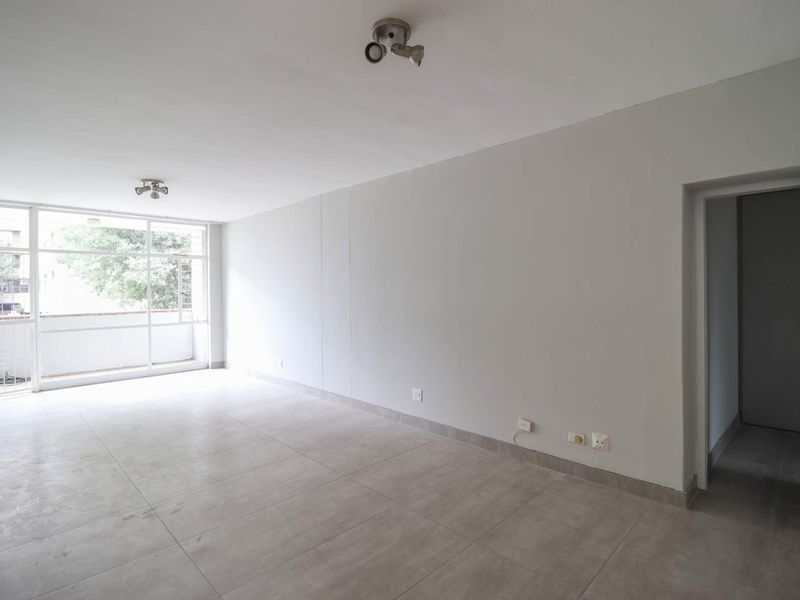 A bright, empty living room featuring neutral tiled flooring, modern ceiling spotlights, and a large glass sliding door leading to an outdoor balcony area.