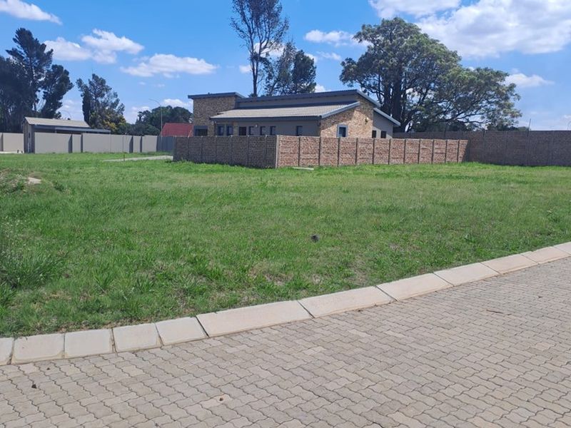 A vacant residential plot featuring a paved driveway, established grass lawn, and brick boundary walling, offering a clear space for future development.