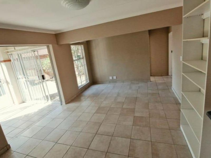 An open-plan living area featuring neutral tiled flooring, built-in shelving, and a sliding glass door providing access to the exterior.