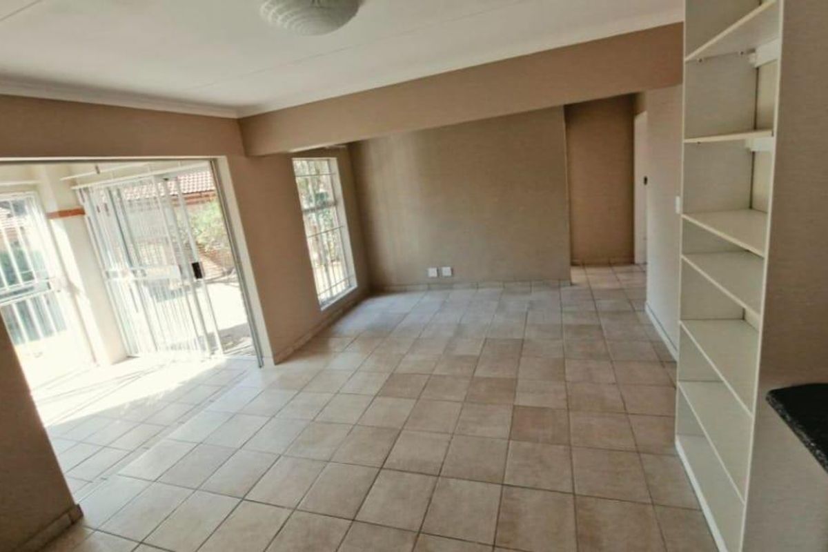 An open-plan living area featuring neutral tiled flooring, built-in shelving, and a sliding glass door providing access to the exterior.