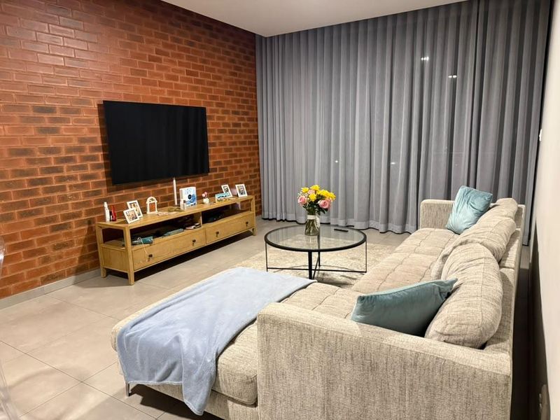 A modern living room featuring a striking exposed brick feature wall, neutral tiled flooring, and expansive floor-to-ceiling curtains for a sophisticated, cozy atmosphere.
