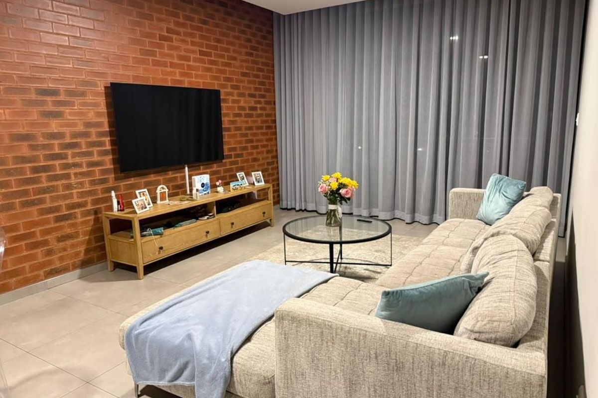 A modern living room featuring a striking exposed brick feature wall, neutral tiled flooring, and expansive floor-to-ceiling curtains for a sophisticated, cozy atmosphere.