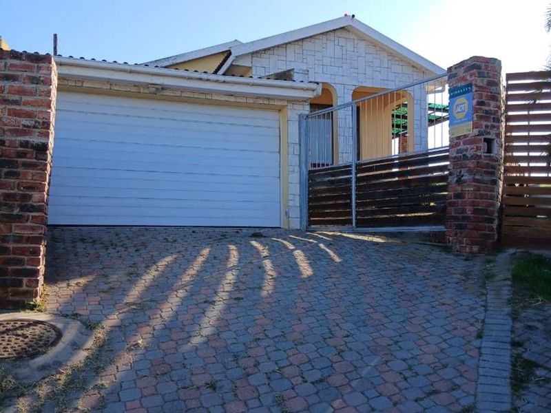 Front exterior view of the property featuring a paved driveway, garage door, and gated entrance with stone cladding accents.