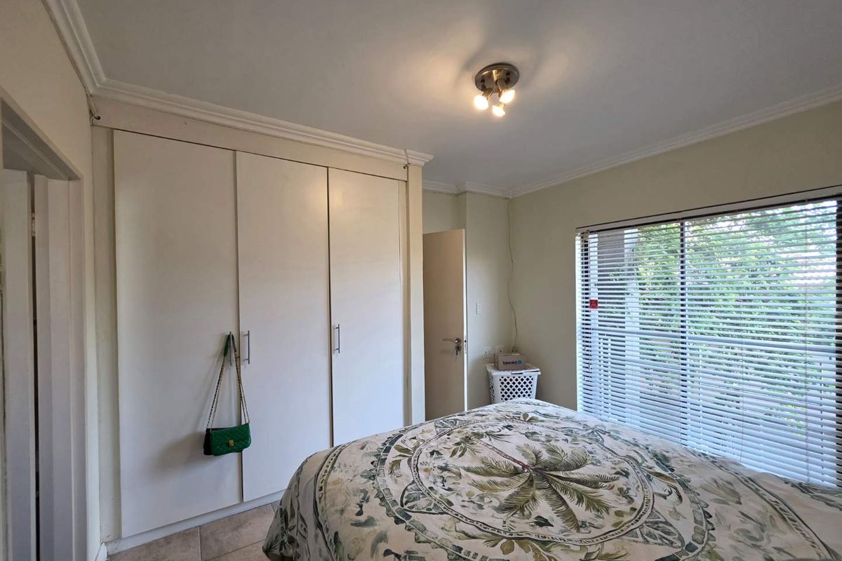 A bedroom featuring built-in cupboards, tiled flooring, and venetian blinds, offering a functional space with neutral finishes.
