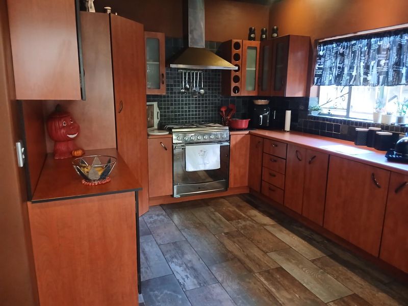 A functional kitchen featuring warm-toned wooden cabinetry, a stainless steel gas stove with extractor fan, tiled backsplash, and durable wood-look flooring.