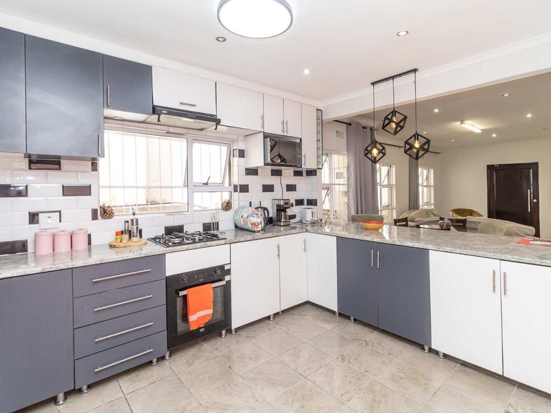 Modern kitchen featuring two-tone cabinetry, granite countertops, subway tile backsplash, and integrated appliances, with an open-plan layout connecting to the living area.