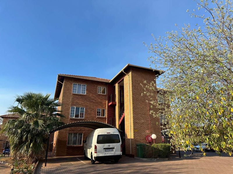 Exterior view of a multi-story face brick apartment building featuring a paved driveway and covered carport parking area.
